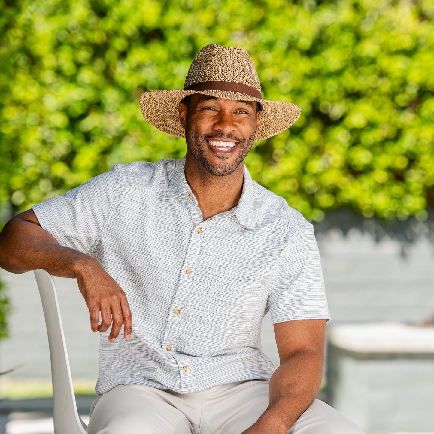 Man wearing the Outback UPF 50+ sun hat and light shirt sitting outdoors with greenery in the background, Brown