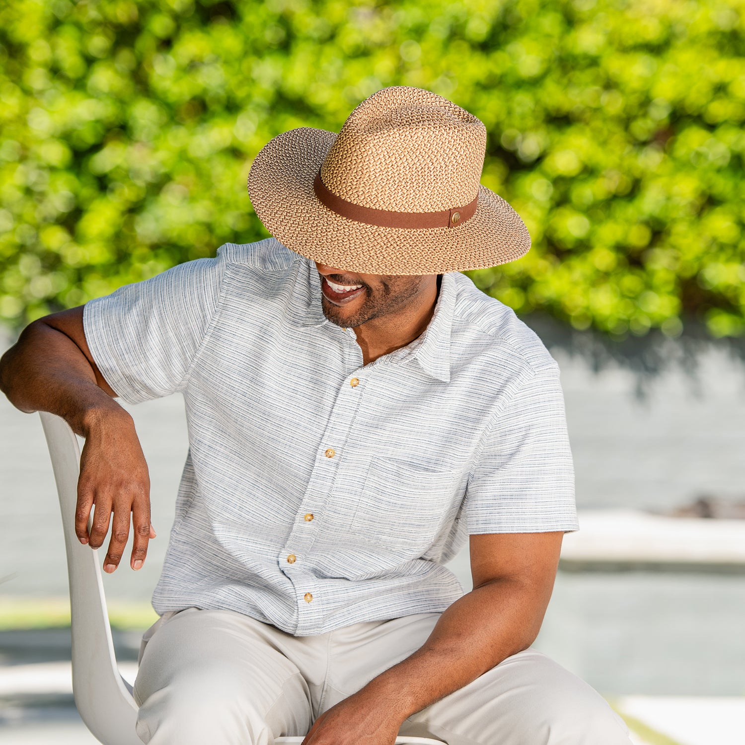 Man wearing the Outback UPF 50+ sun hat and light shirt sitting outdoors with greenery in the background, Brown