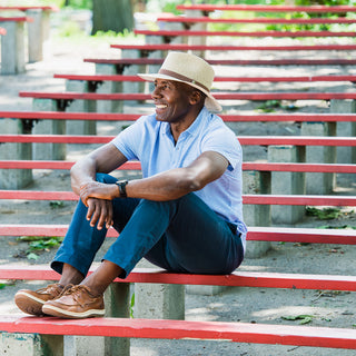 Man sitting at a festival, wearing the Wallaroo Outback wide brim sun hat, providing sun protection with natural fibers, perfect for an active day in the city’s natural landscapes, Natural