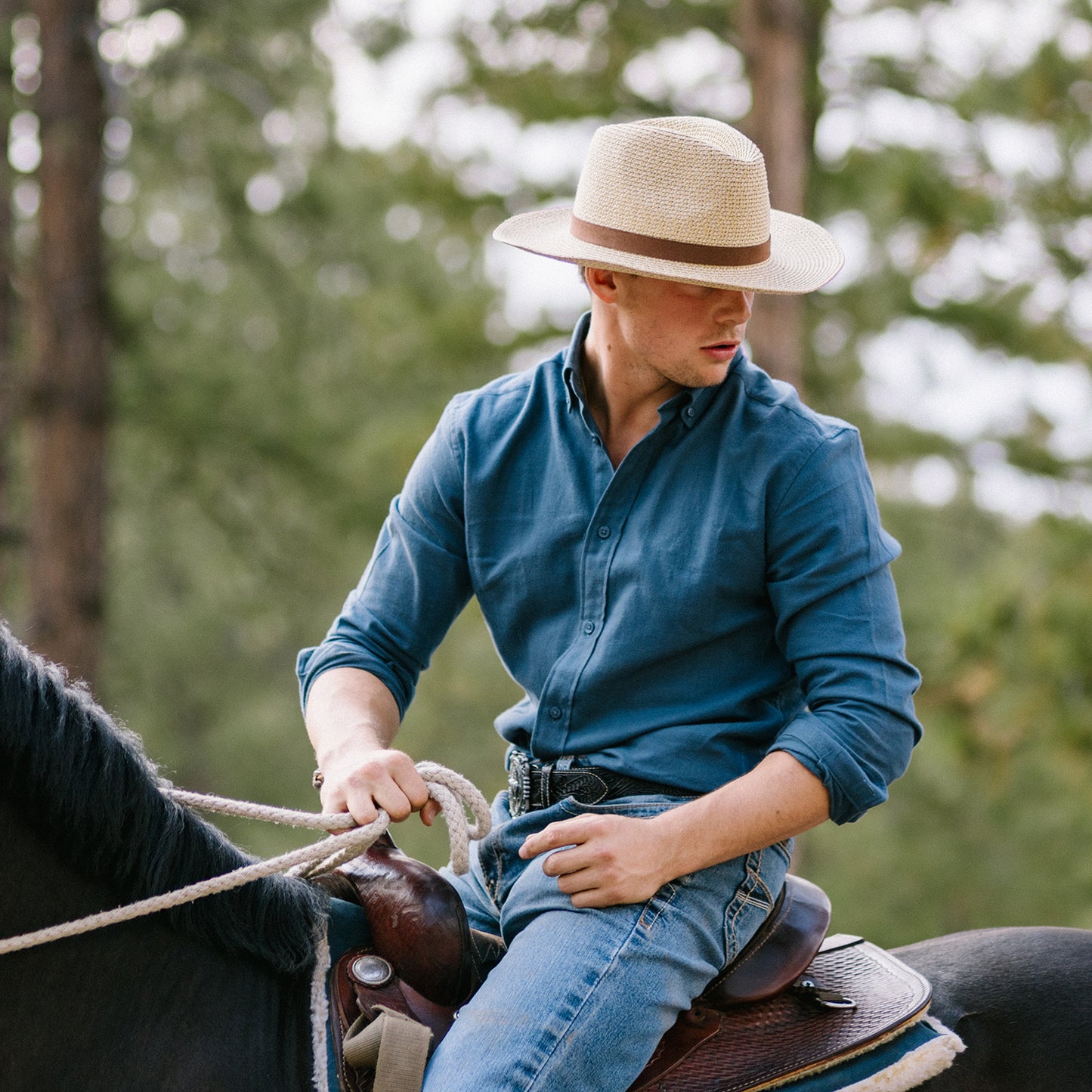 Man riding a horse wearing the Outback fedora sun hat in a forested area, Natural