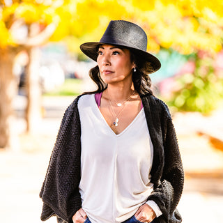 Woman strolling on a city street, wearing the Wallaroo Palm Beach wide brim sun hat, combining sun protection with a relaxed, stylish outdoor look, Black