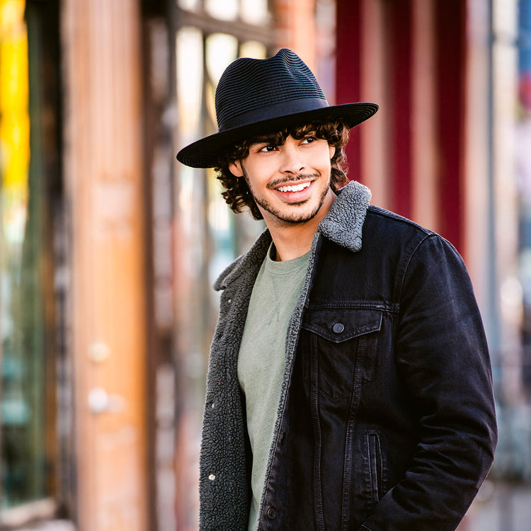 Man in the city, wearing the Wallaroo Palm Beach wide brim sun hat, perfect for sun protection in natural landscapes with a stylish edge, Black