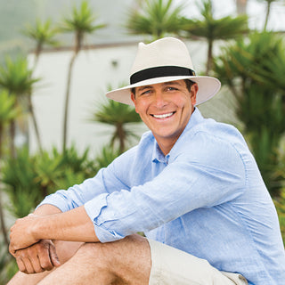 Man sitting by a pool, wearing the Wallaroo Palm Beach wide brim sun hat with UPF 50 protection, perfect for enjoying outdoor spaces, Ivory