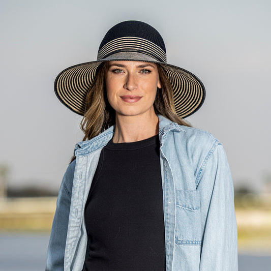 Woman wearing a wide-brimmed Petite Marseille UPF 50+ sun hat with a striped band against a neutral background