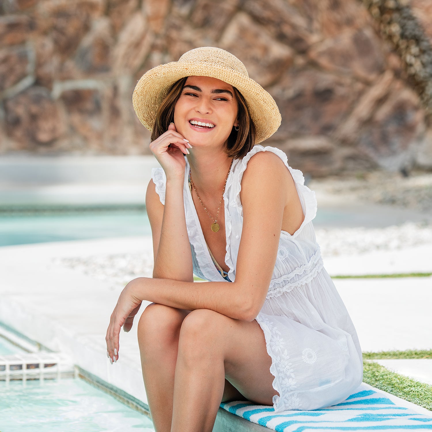 Woman sitting by a pool with a petite catalina straw sun hat with upturned brim by Wallaroo designed for smaller sized heads, Natural
