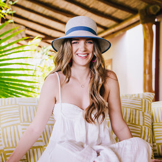 Woman relaxing on a patio wearing the Wallaroo Petite Darby Sun Hat, designed for small heads, featuring a wide brim, UPF 50+ sun protection, and a graceful round crown in Ivory/Dusty Blue