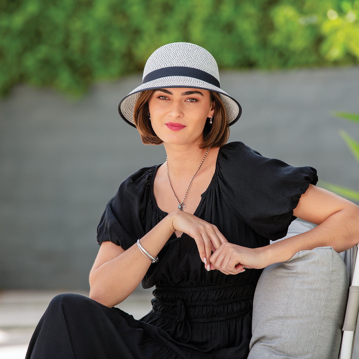 Woman wearing women's Petite Darby cloche bucket travel sun hat sitting on a chair, Ivory/Black