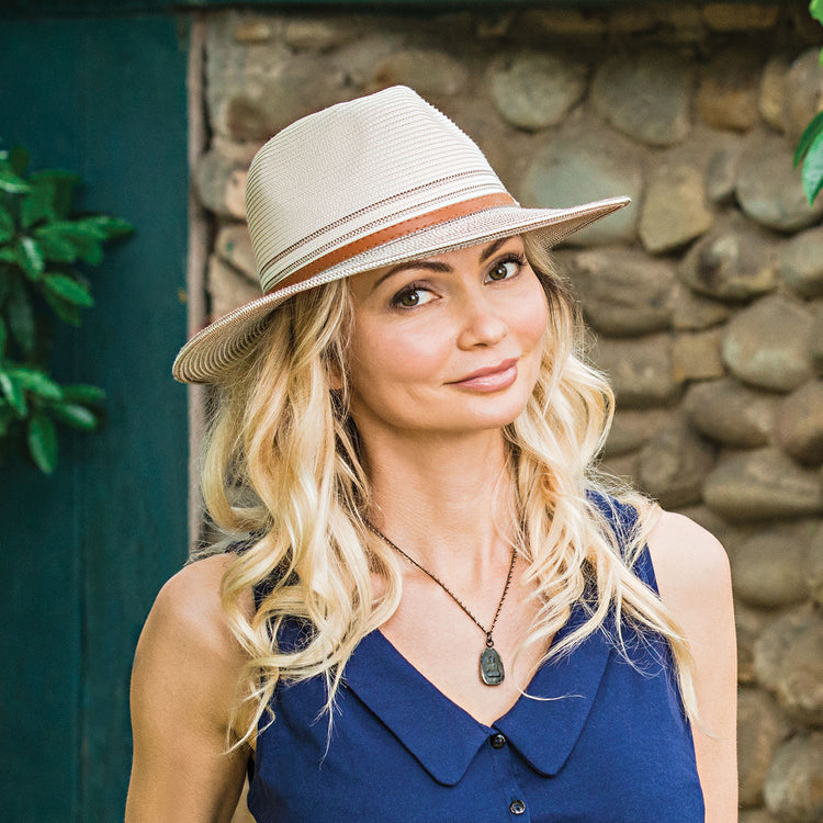 Woman taking a garden walk, wearing the Wallaroo Petite Kristy Fedora Sun Hat, offering UPF 50+ protection and a wide brim design, perfect for active outdoor excursions, Ivory/Stone