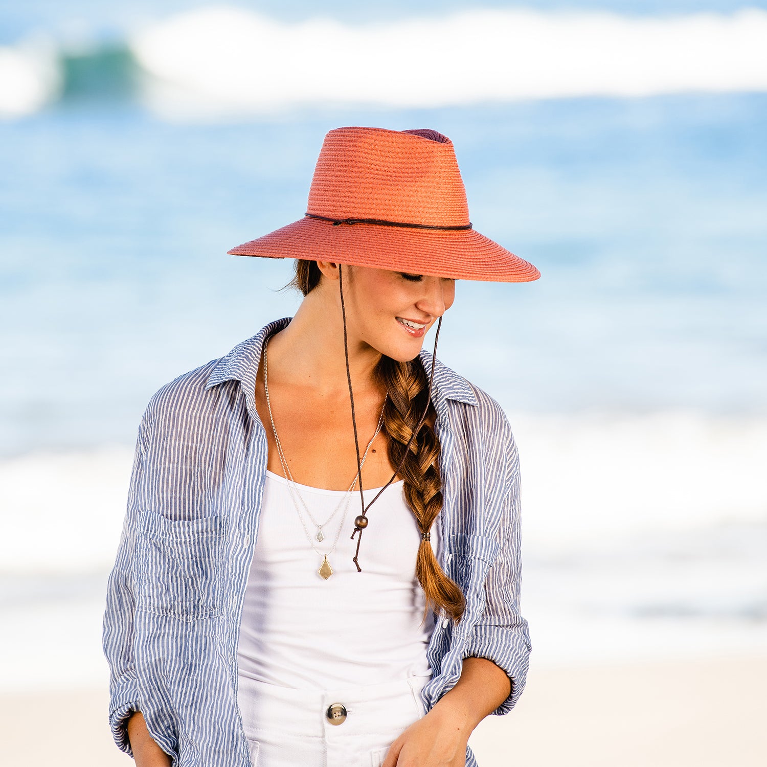 Woman enjoying a beachside brunch, wearing the Wallaroo Petite Sanibel wide brim sun hat, designed to protect petite heads with UPF 50+ sun protection and chin strap, Coral