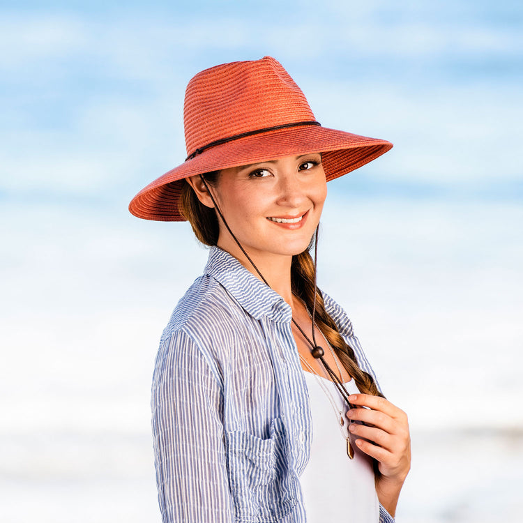 Woman exploring a tropical island, wearing the Wallaroo Petite Sanibel wide brim sun hat, offering lightweight sun protection and a comfortable fit for small heads in warm climates, Coral