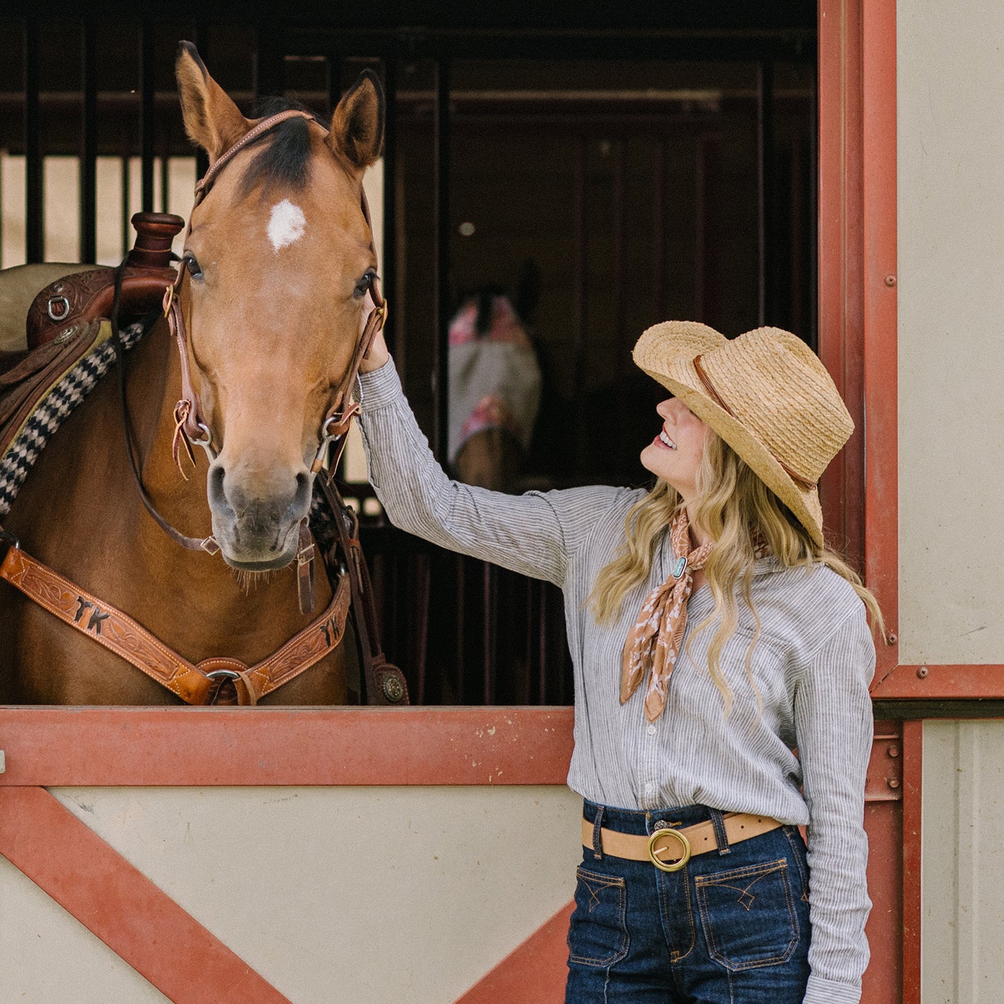 Woman wearing Quinn raffia cowboy hat standing with a horse in a barn. 