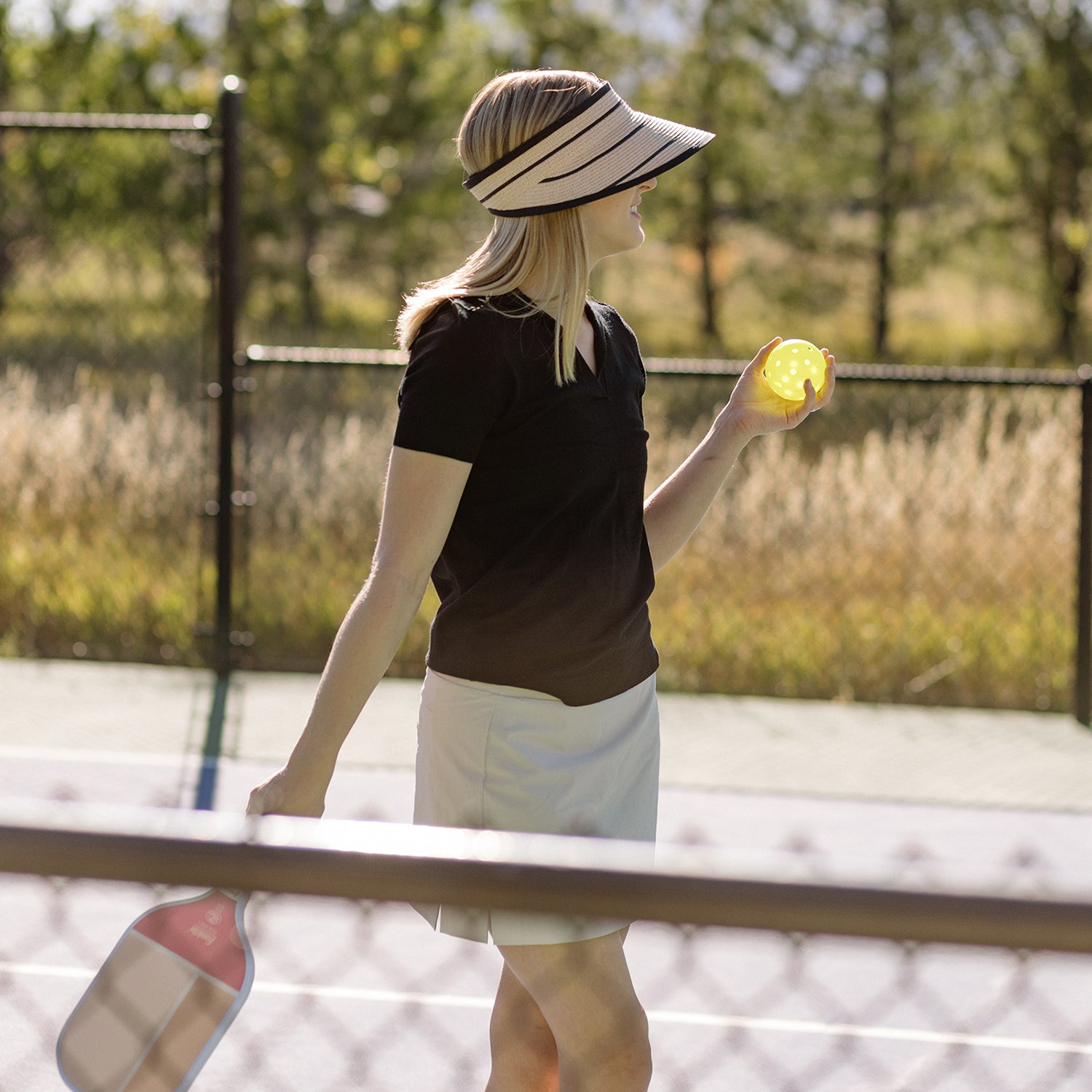 Woman enjoying a game of pickleball at a resort, shaded by the Wallaroo Savannah Wide Brim Sun Visor, designed for active sports and sunny summer afternoons, Camel/Black