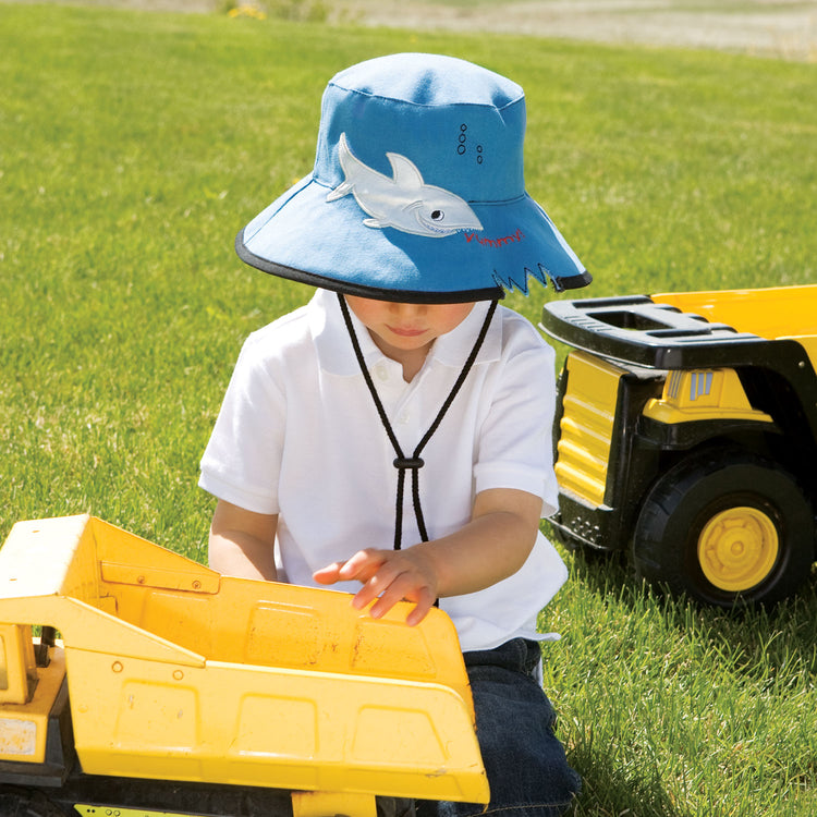 Child playing, shaded by the Wallaroo Children's Shark Sun Hat, featuring a durable wide brim and UPF 50+ for long days in the sun, Blue