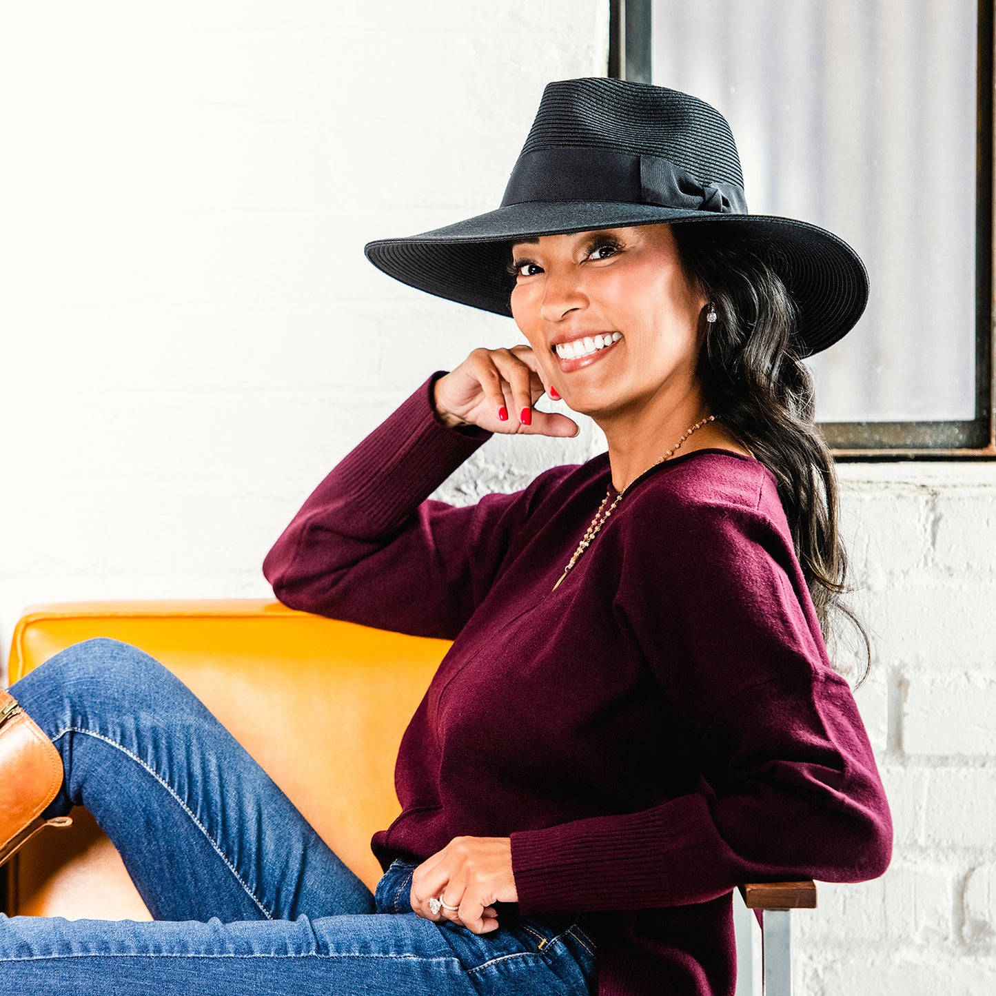 Woman wearing a St. Lucia black hat and maroon sweater sitting on an orange chair.