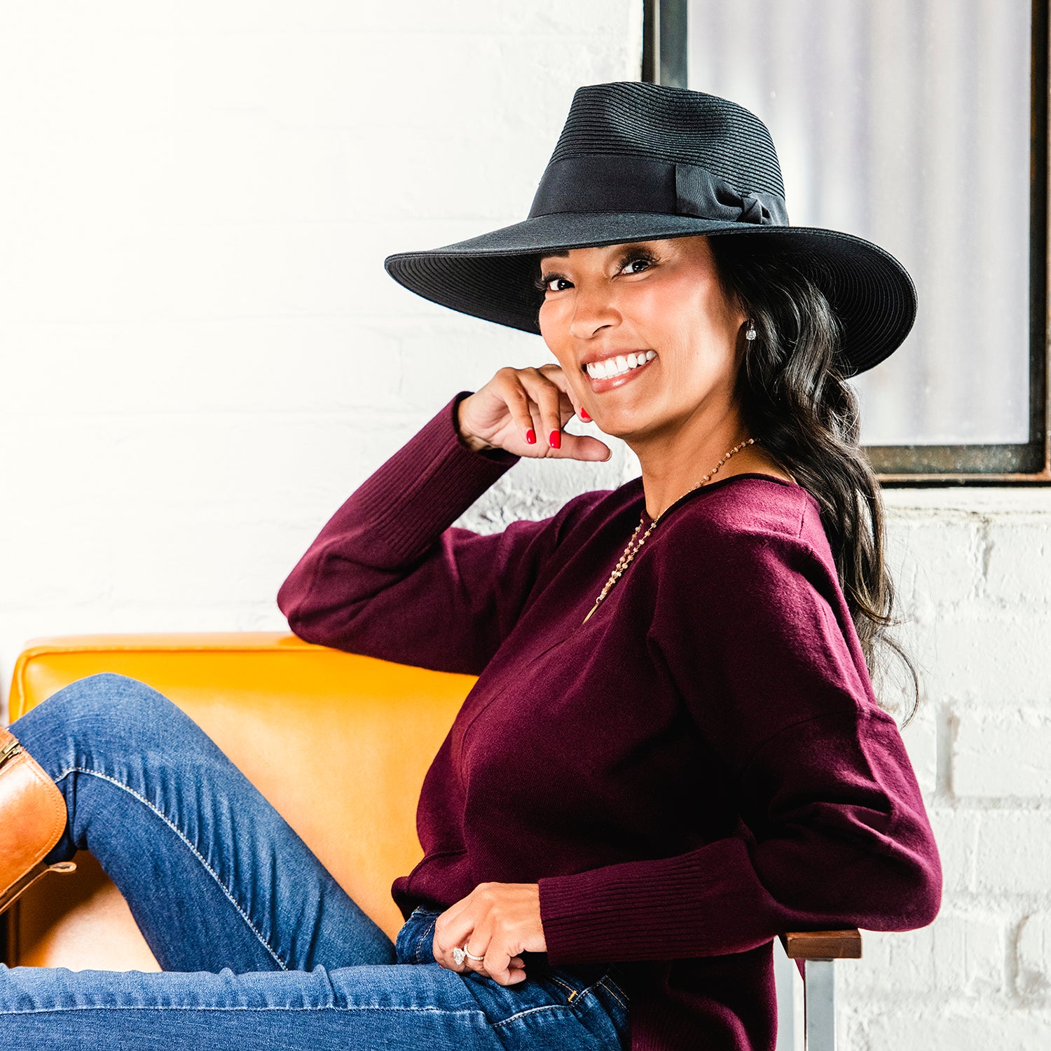 Woman wearing a St. Lucia black hat and maroon sweater sitting on an orange chair.