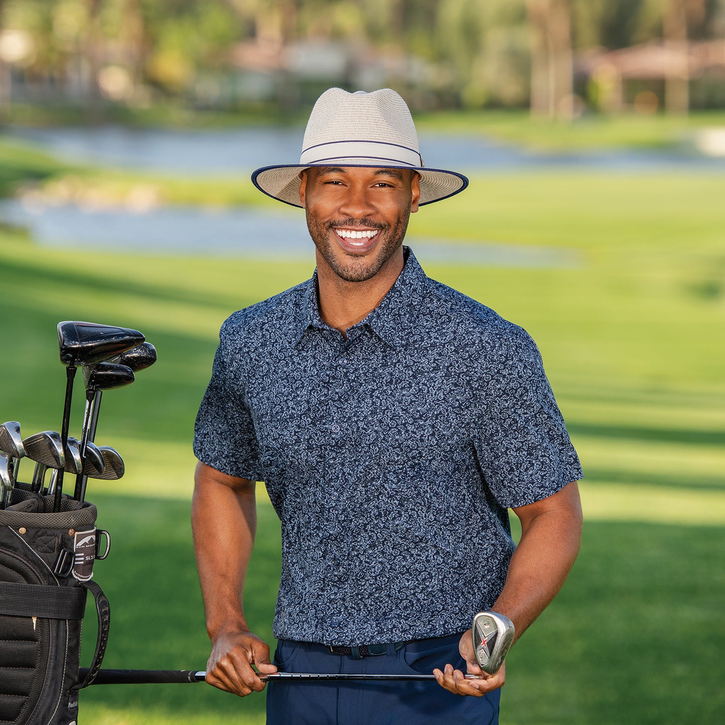 Man holding a golf club and smiling on a golf course wearing Sterling, mixed camel.