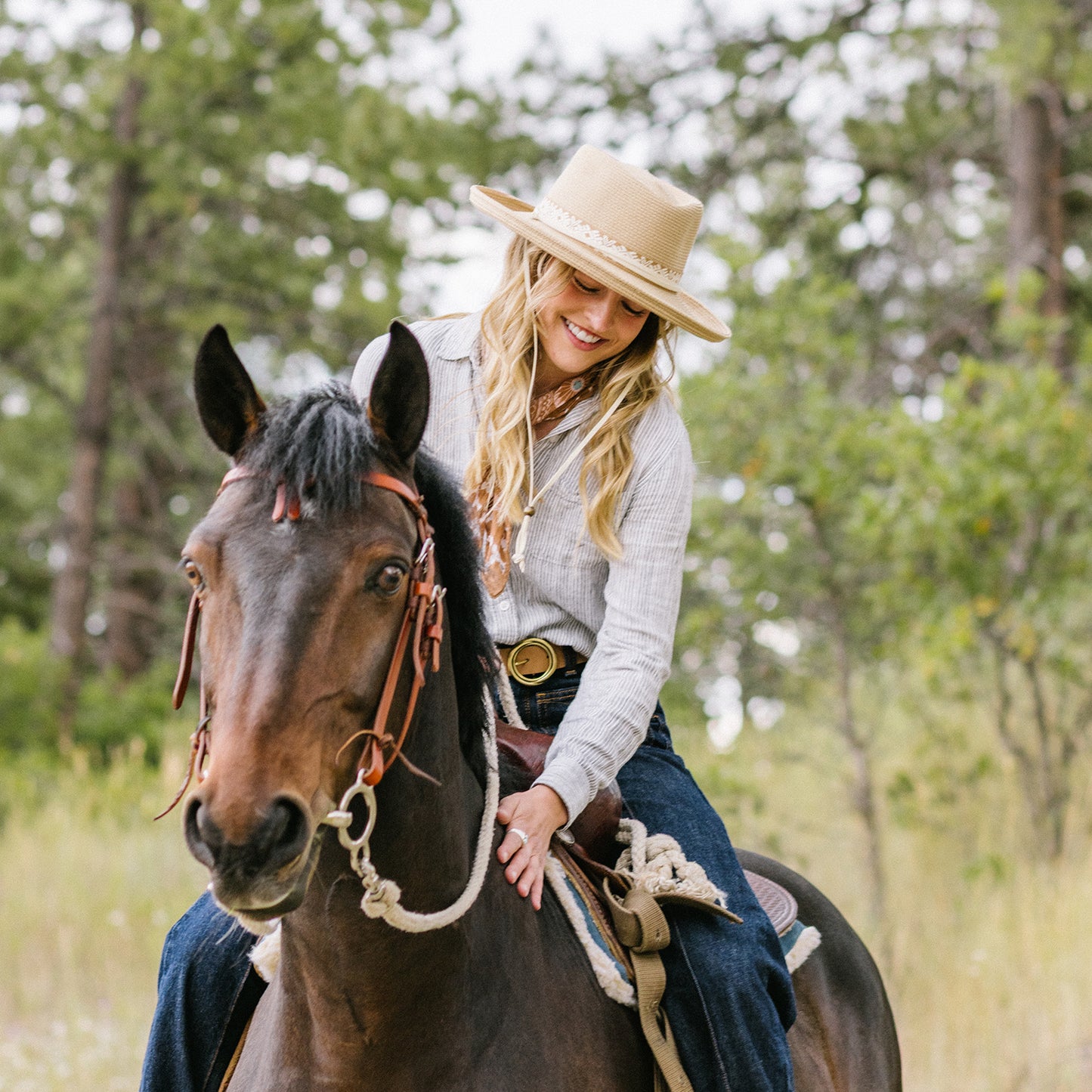 Woman wearing Stevie fedora with chinstrap riding a horse in a forested area, Camel