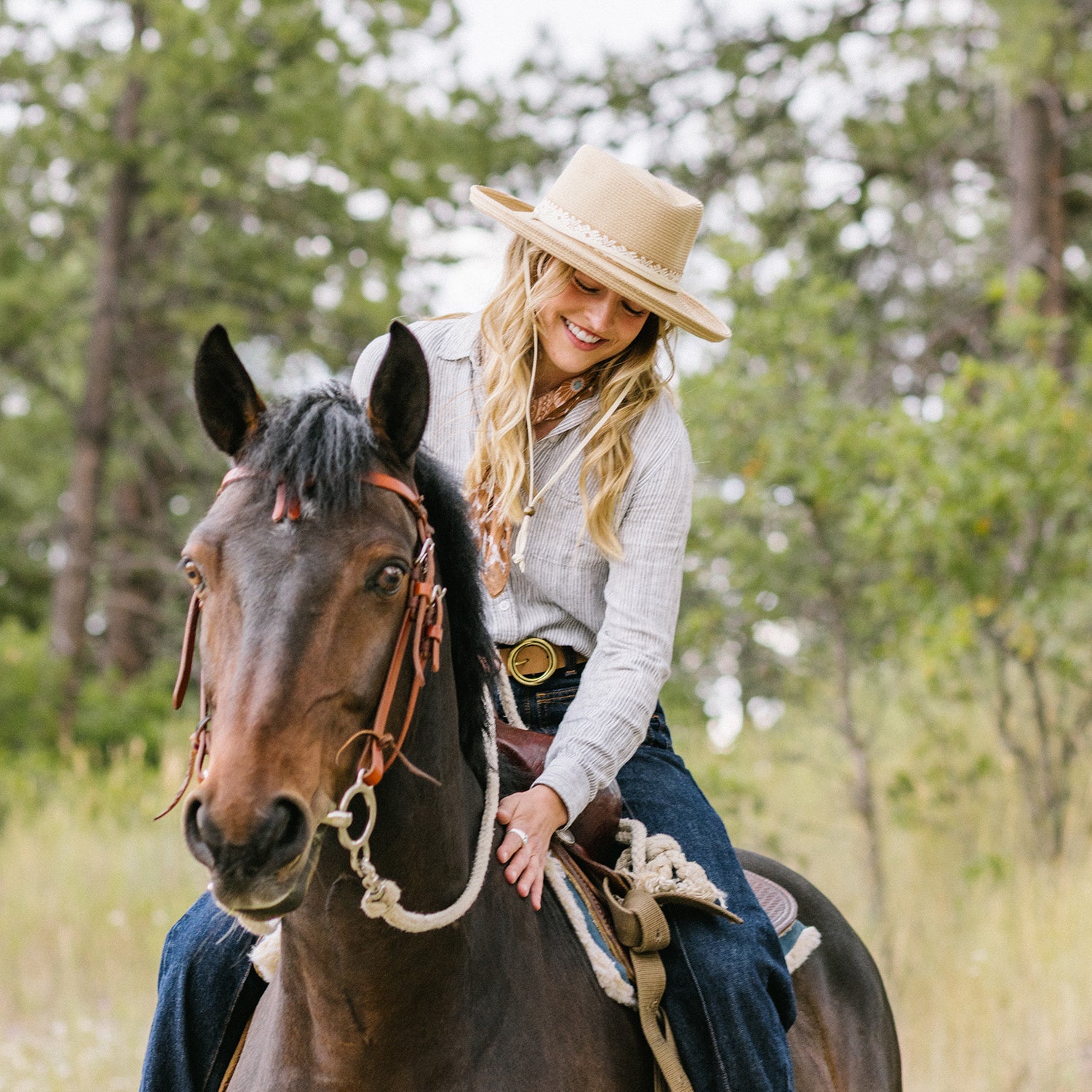Woman wearing Stevie fedora with chinstrap riding a horse in a forested area, Camel
