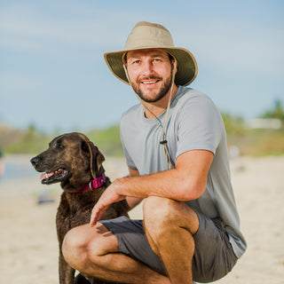 Man playing with his dog staying cool under the Wallaroo Men’s Summit Bucket Hat, featuring a wide brim and chin strap for windy days, Khaki