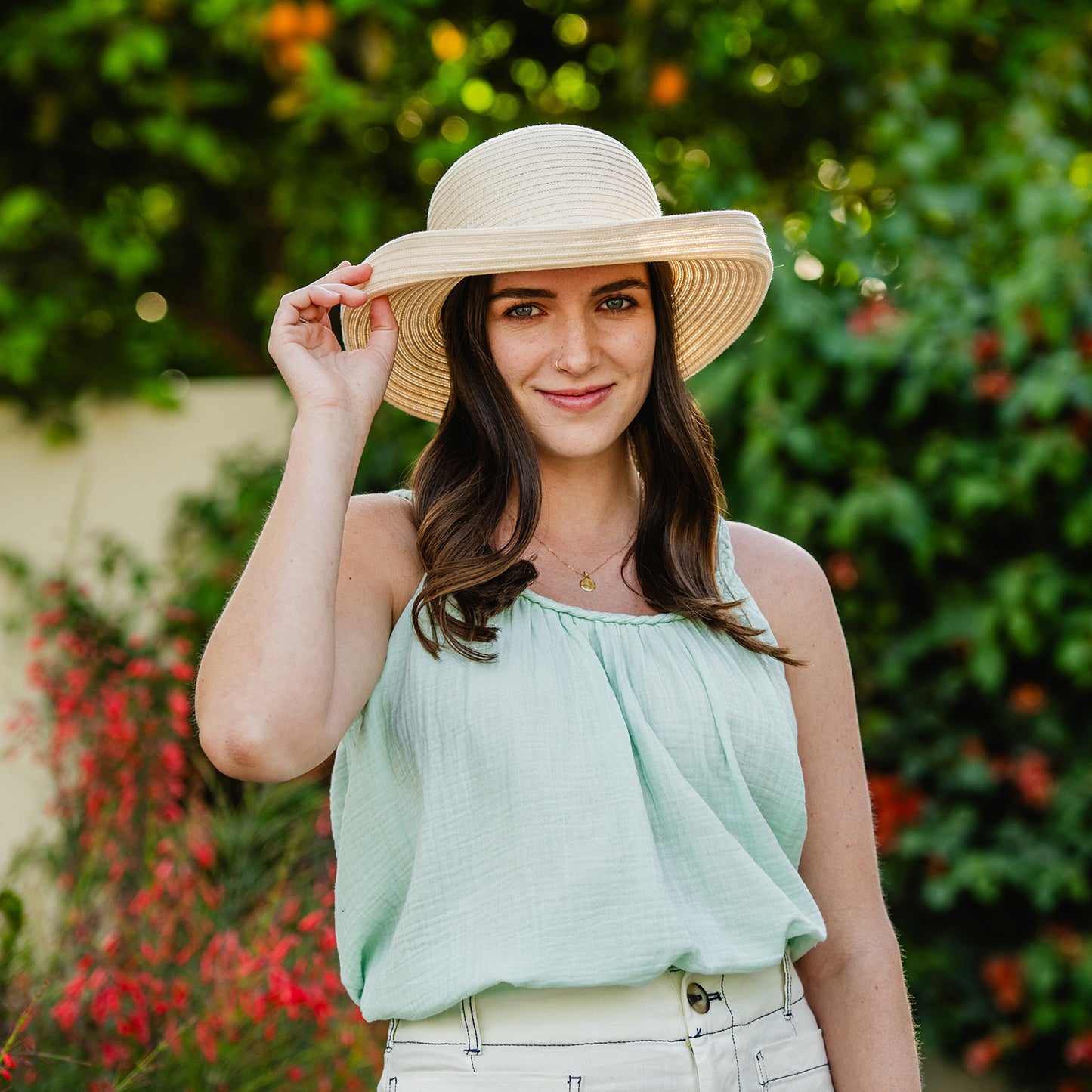 Woman wearing a Sydney sun hat and light green top outdoors with greenery in the background, Ivory