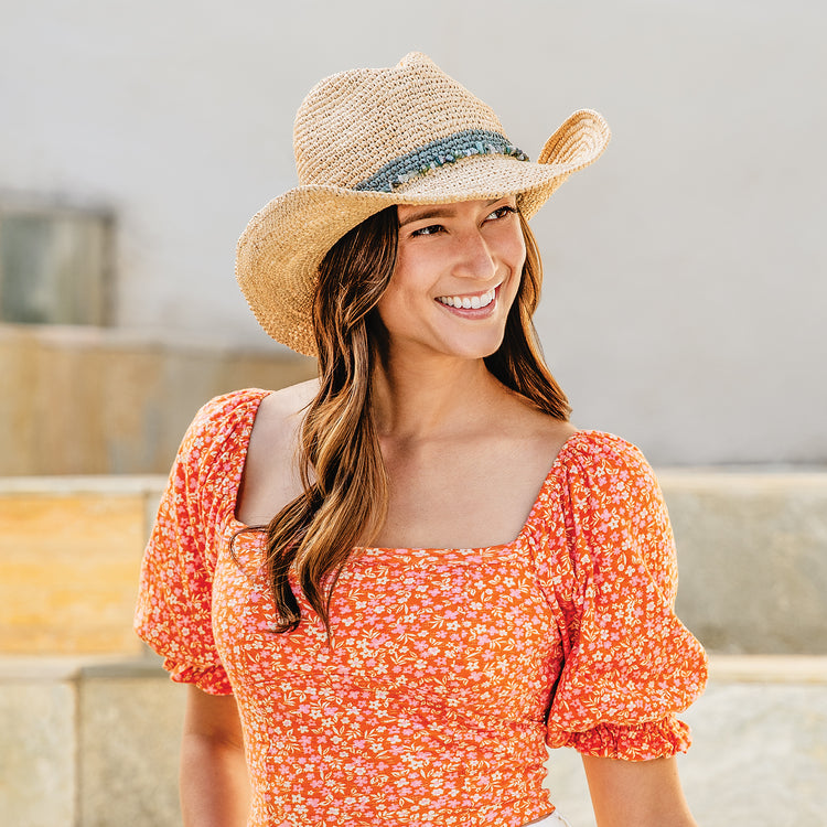 Woman at a mountain lodge, shaded by the Wallaroo Tahiti Cowboy Hat, a raffia straw sun hat designed for resort life and warm summer afternoons, Sage