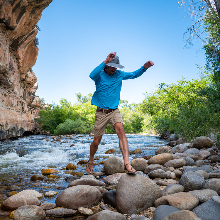 Man wearing the Carkella Tahoe water-resistant wide brim packable hat, enjoying the outdoors by a creek, showcasing UV protection and comfort for outdoor adventures and travel, Dark Grey/Stone