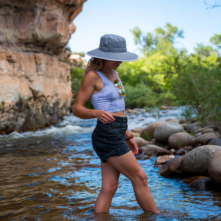 Woman wearing the Carkella Tahoe water-resistant wide brim packable hat, exploring a creek, with UV protection and a stylish, practical design perfect for outdoor adventures and travel, Dark Grey/Stone