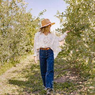 Woman hiking a scenic mountain trail, wearing the Wallaroo Women’s Telluride Fedora Sun Hat, crafted from SPF 50 faux suede for stylish sun protection on hot summer days, Camel