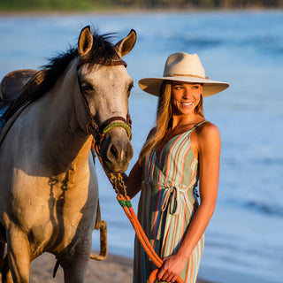 Woman with a horse on a scenic beach wearing the Wallaroo Tulum Cowboy Hat, offering breathable comfort and sun protection during outdoor adventures, Natural