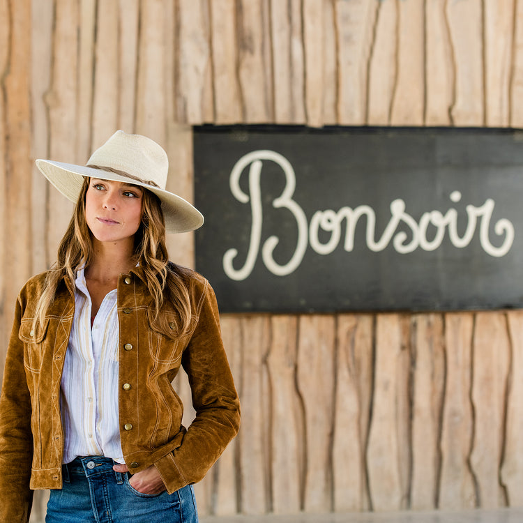 Woman at a café in Malibu, shaded by the Wallaroo Tulum Cowgirl Sun Hat, a lightweight raffia straw hat designed for stylish summer mornings, Natural