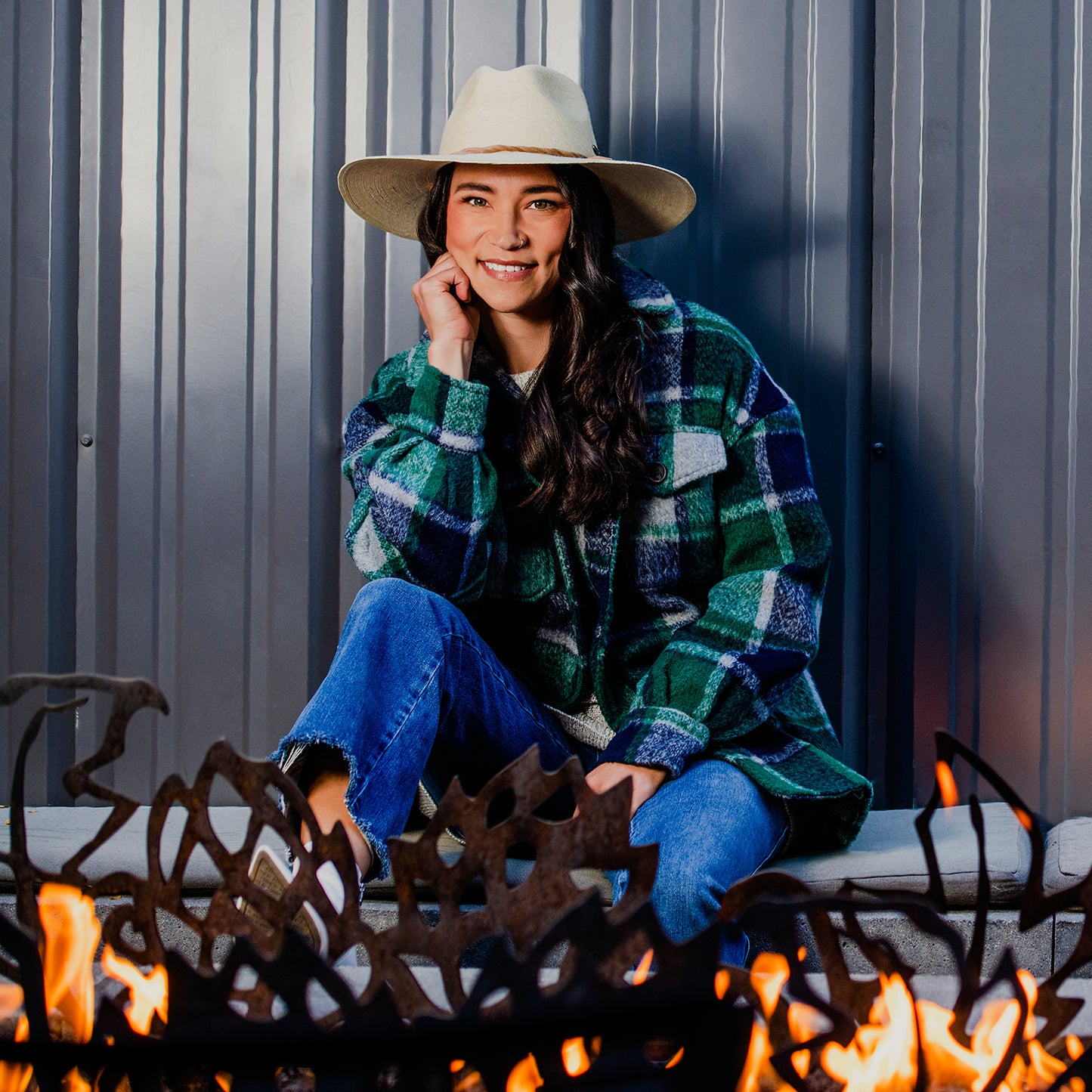 Woman wearing natural fiber Tulum wide brim UPF 50+ hat for year-round wear, sitting in front of a fire pit, Natural