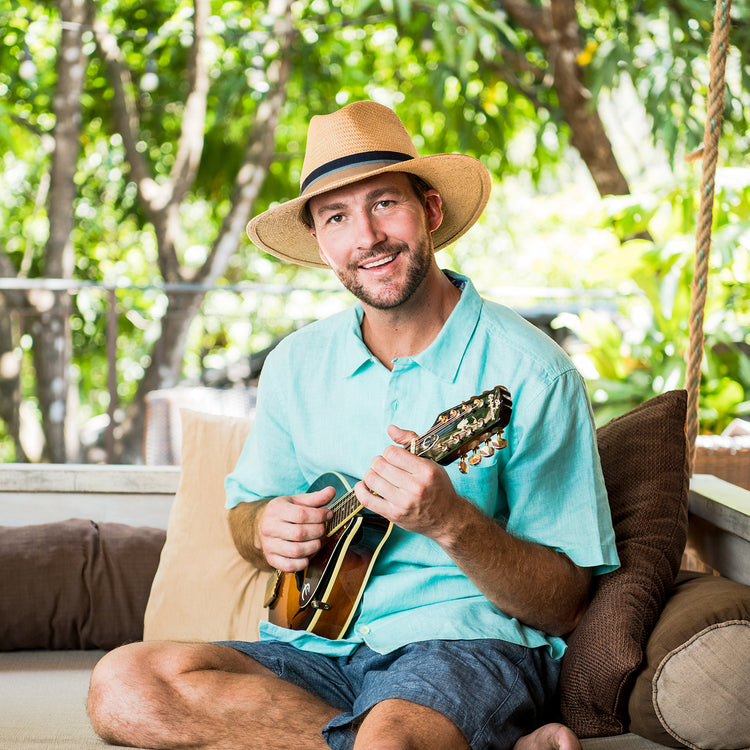 Man performing at an open-air music festival, wearing  the Wallaroo Turner Sun Hat, an elegant natural straw hat ideal for summer events, Camel