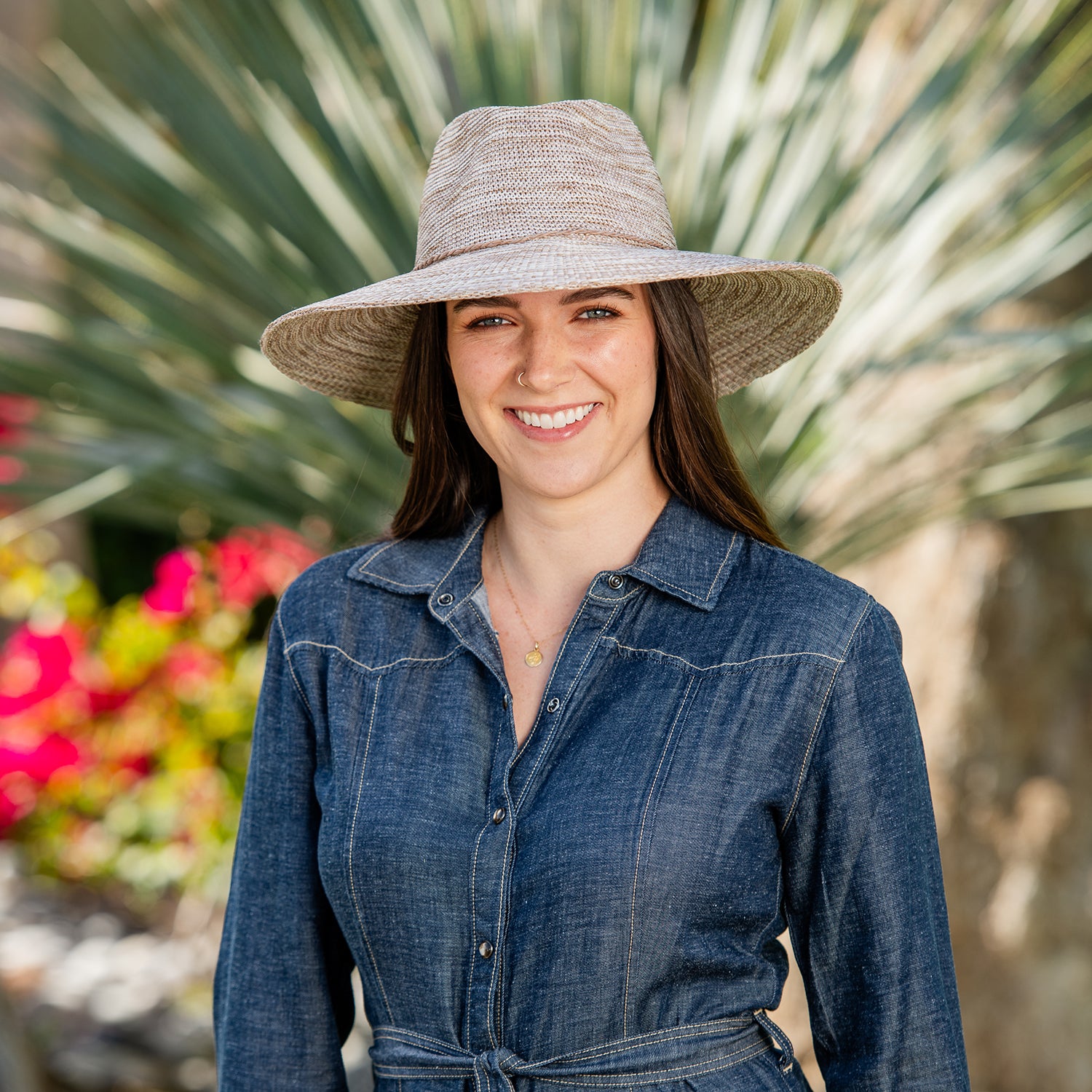 Woman wearing a denim dress and Victoria Fedora Diva wide-brimmed sun hat with a blurred natural background, Mixed Camel