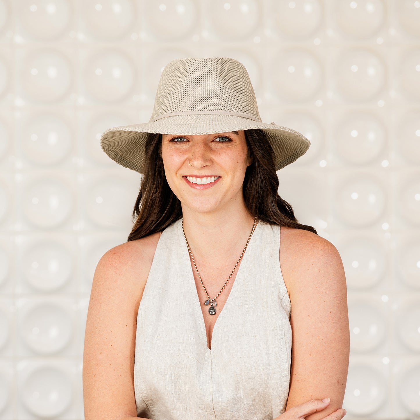 Woman wearing a Victoria Fedora sun hat and white sleeveless top against a textured wall, Stone