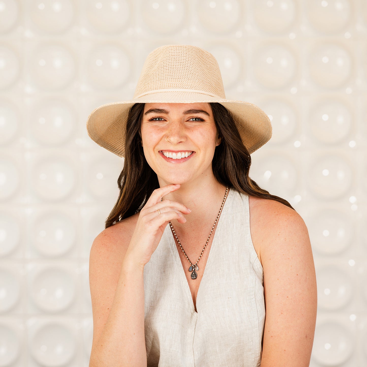 Woman wearing the Victoria Fedora sun hat against a textured white background, tan