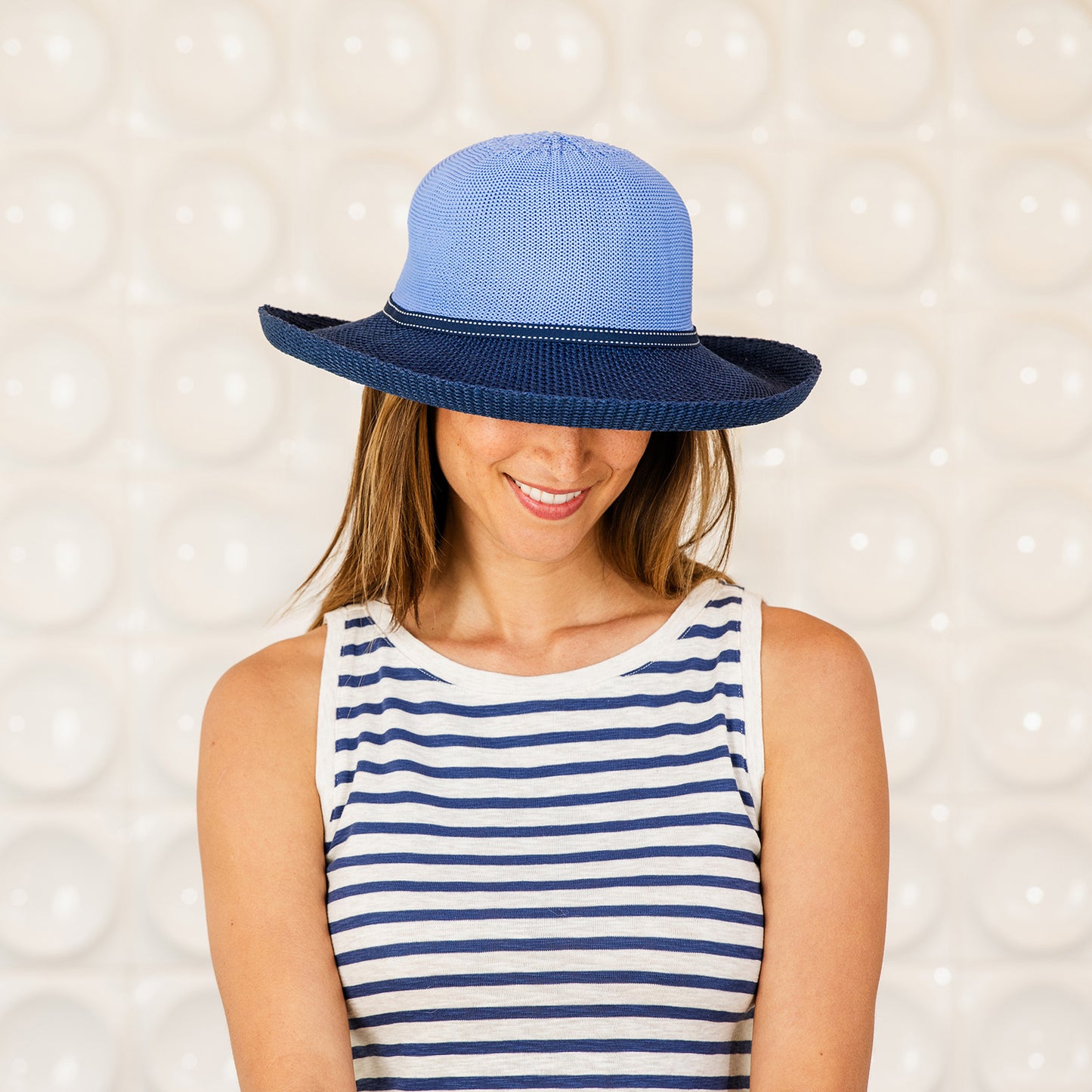 Woman wearing a Victoria Two-Toned  wide-brimmed sun protection hat against a textured wall, Hydrangea/Navy