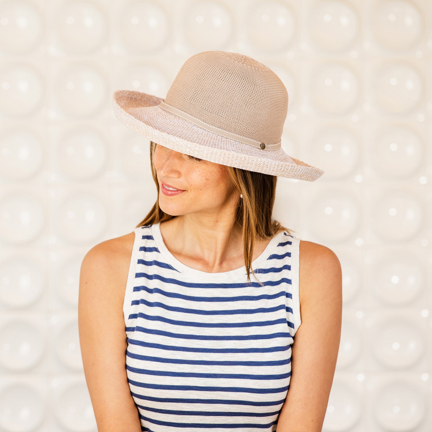 Woman wearing a Victoria Two-Toned sun hat and striped tank top against a textured wall, Latte/Mixed Beige