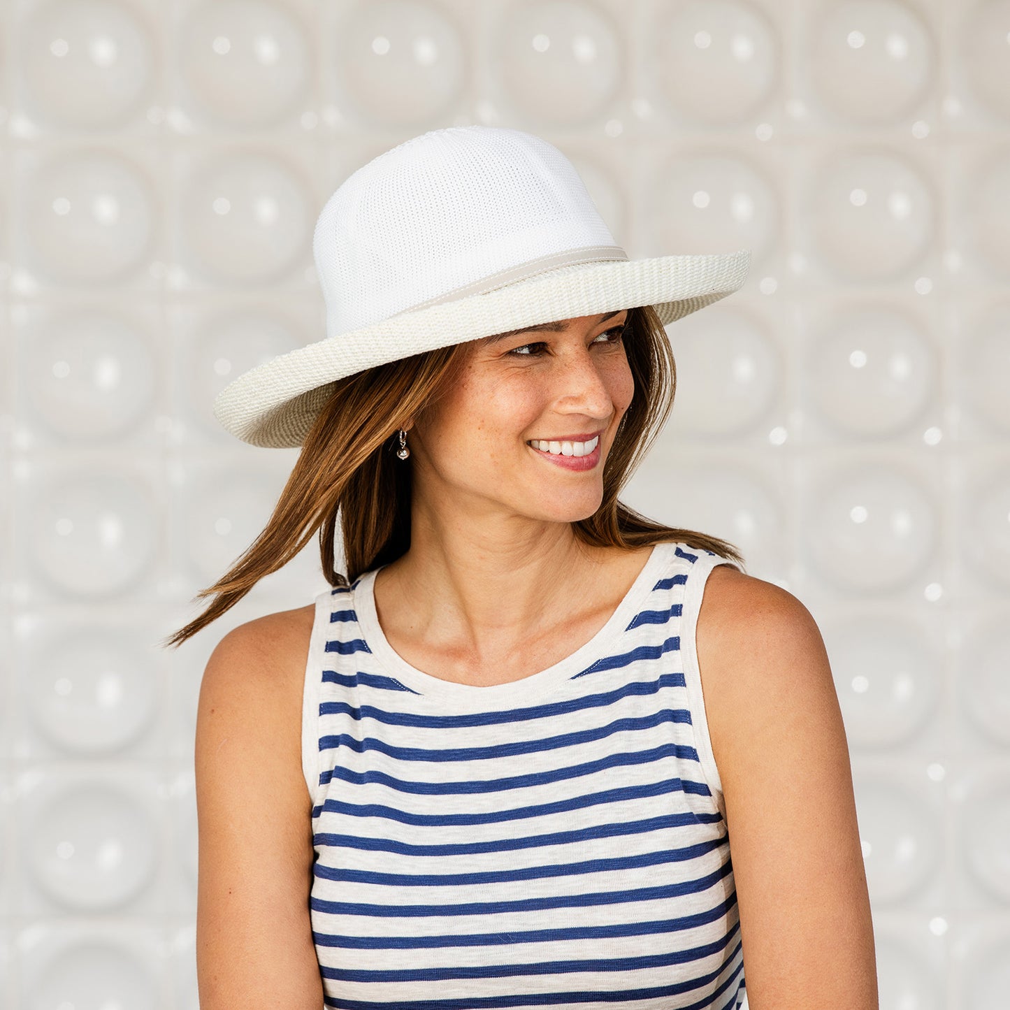 Woman wearing a Victoria Two-Toned sun protection hat and striped tank top against a textured white background, White/Natural