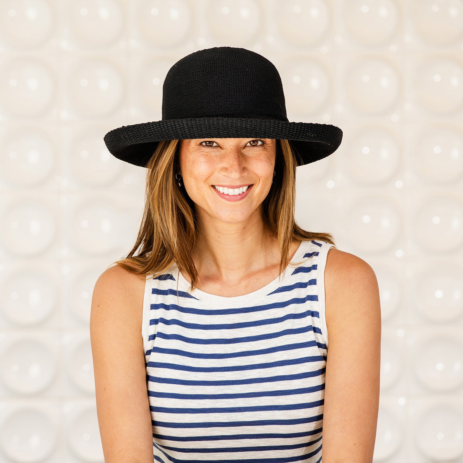 Woman wearing a Victoria UPF sun protection hat and striped tank top against a textured white background, Black