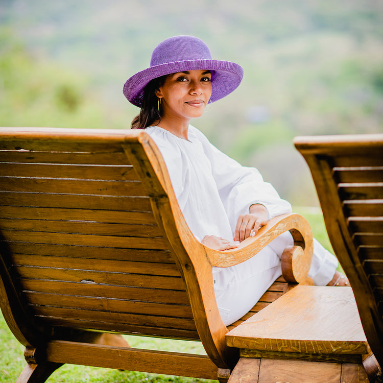 Woman taking in the view from a resort balcony, wearing the Wallaroo Victoria Sun Hat, a best-selling poly-straw hat perfect for sunny escapes, 'Deep Lilac'