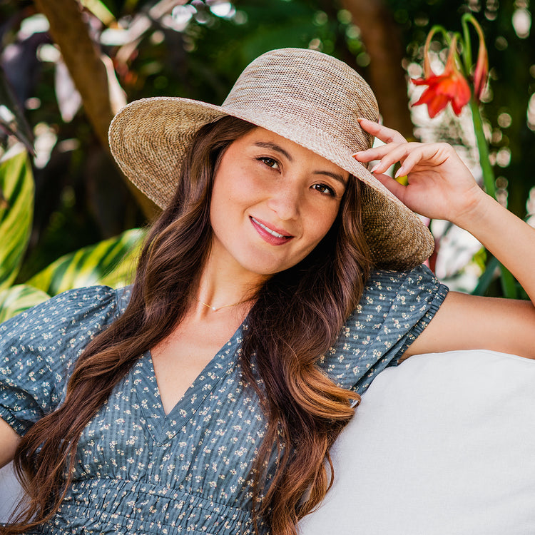 Woman sitting on a resort patio with a stunning view, wearing the Wallaroo Victoria Diva Wide Brim Sun Hat, designed to provide sun protection with an adjustable fit, Mixed/Camel