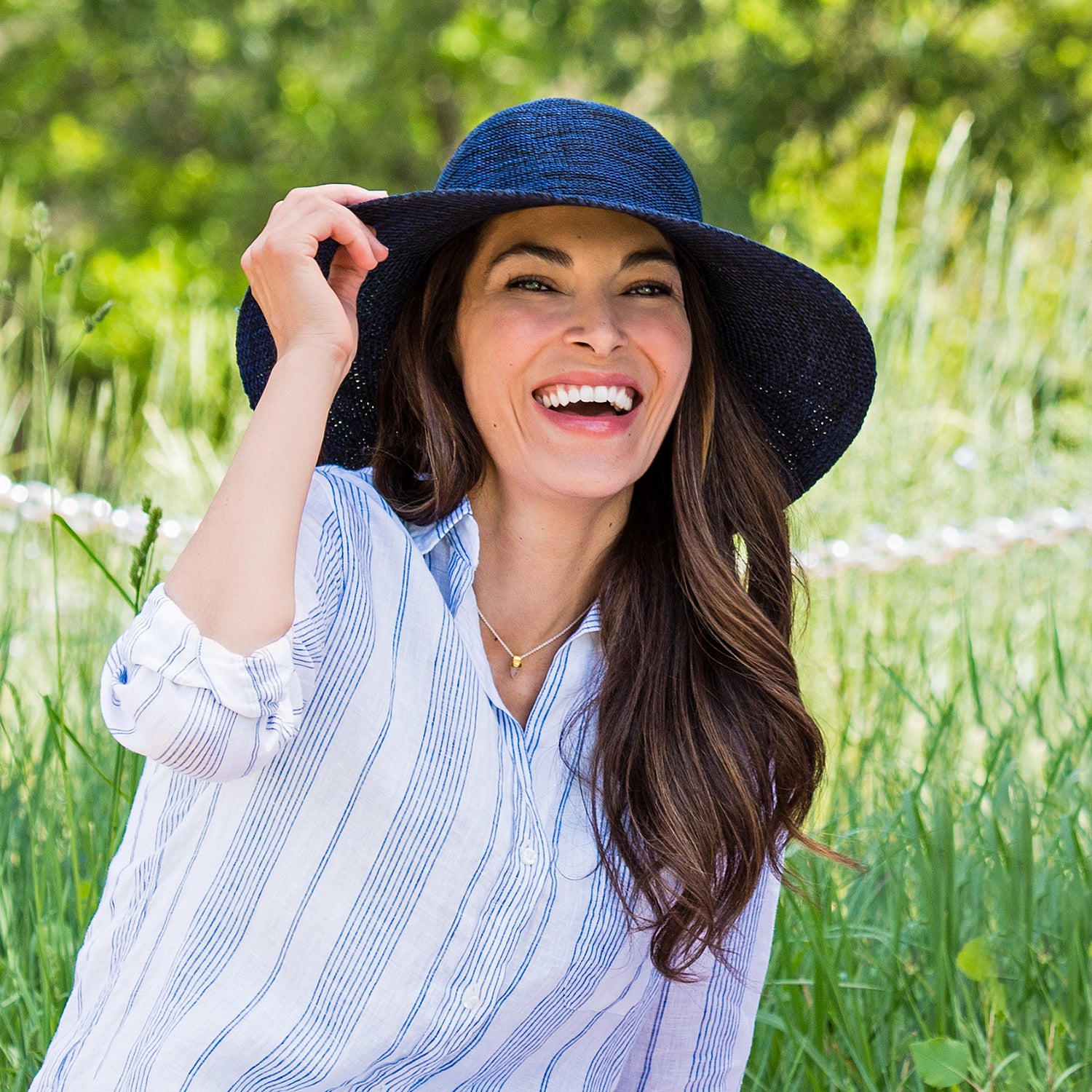Woman enjoying a cool breeze accessorized with the Wallaroo Victoria Diva Wide Brim Sun Hat, crafted from breathable poly-straw for comfort on sunny days, Mixed/Navy