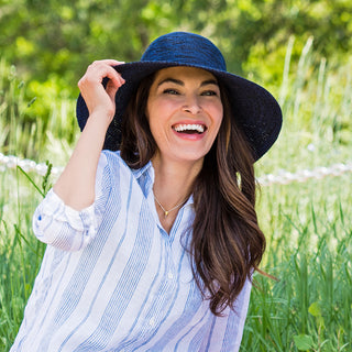 Woman enjoying a cool breeze accessorized with the Wallaroo Victoria Diva Wide Brim Sun Hat, crafted from breathable poly-straw for comfort on sunny days, 'Mixed Navy'