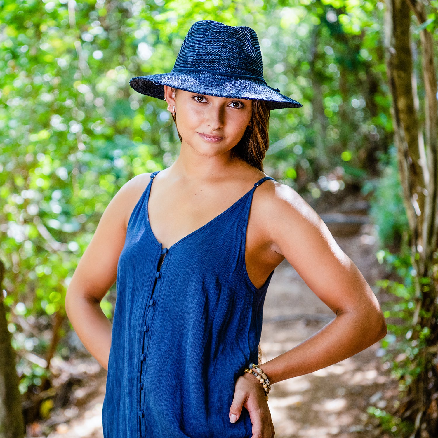 Woman walking along a sunny trail, accessorized with the Wallaroo Victoria Fedora Sun Hat, perfect for summer coastal getaways, Mixed Navy