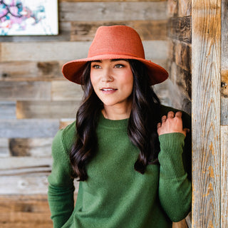 Woman enjoying a mountain resort getaway, wearing the Wallaroo Women’s Victoria Fedora Sun Hat, perfect for combining functionality and elegance in sunny weather, Paprika