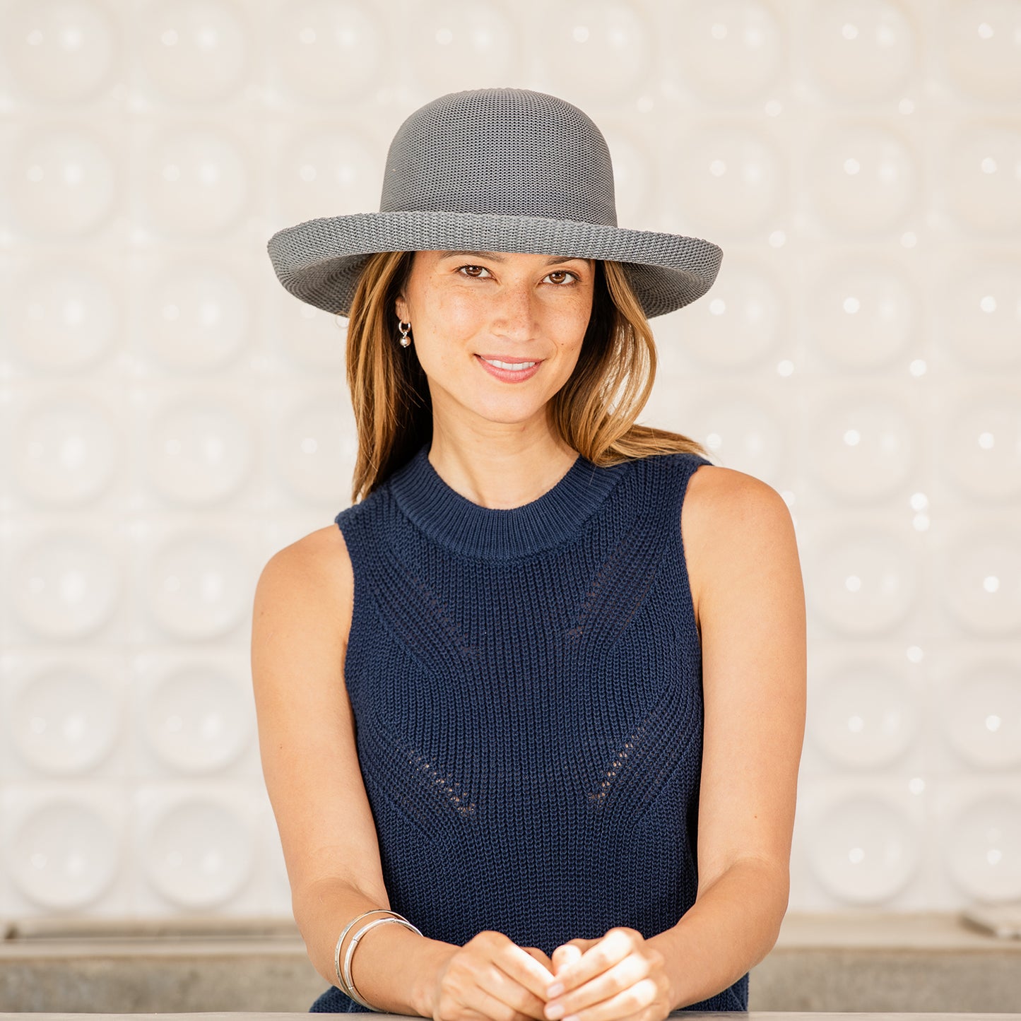 Woman wearing a Victoria sun hat and navy sleeveless top against a light background, Grey