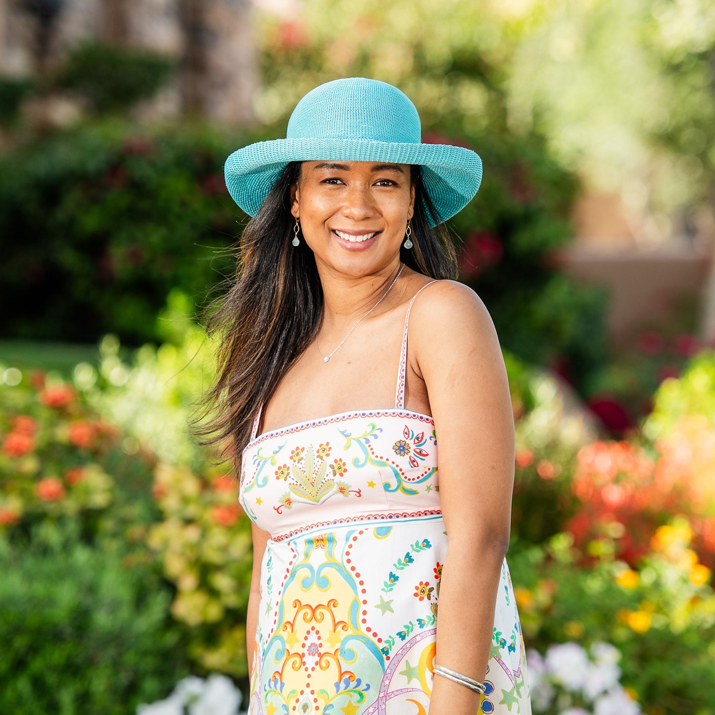 Woman wearing a colorful dress and Victoria sun hat in a garden setting, Jade