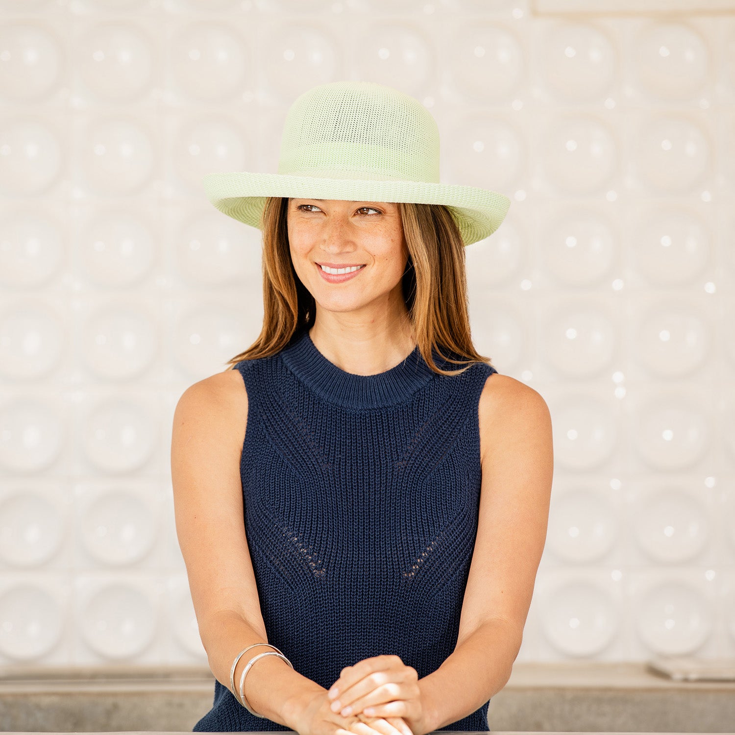 Woman wearing a Victoria sun hat and navy sleeveless top against a textured wall, Lime