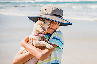 Boy in Junior Explorer hat on the beach holding a dog