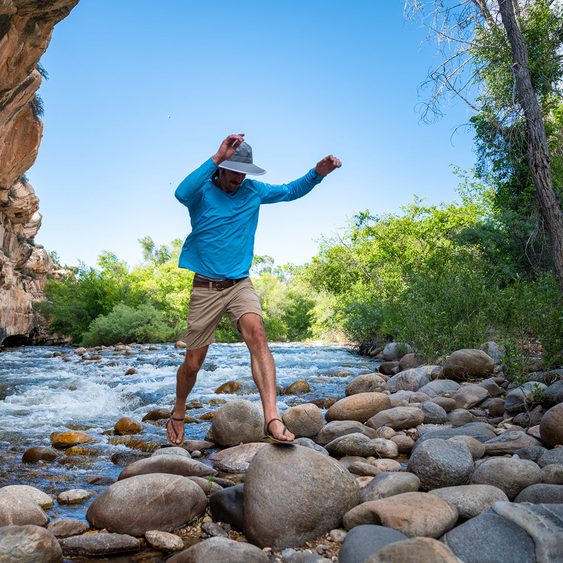 Man stepping over river rocks while wearing Tahoe sun hat by Carkella
